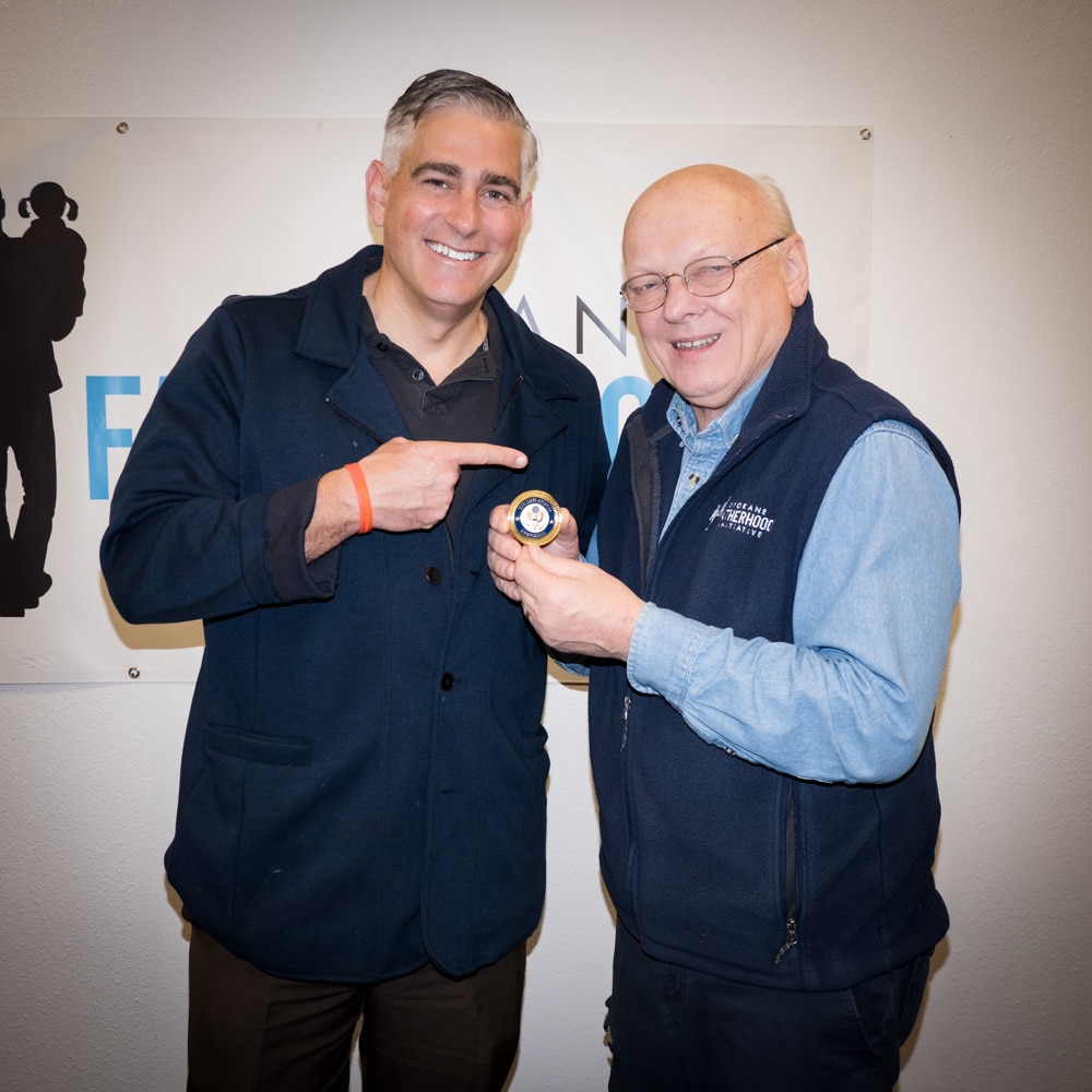Congressman Michael Baumgartner and Ron Hauenstein display a congressional coin at SpoFI offices, both men smiling as they hold the commemorative medal between them