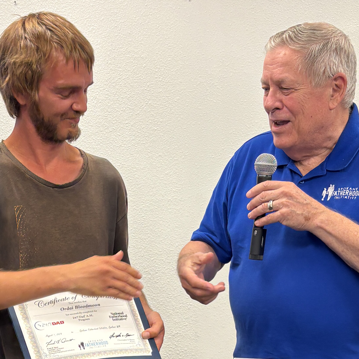 18 Spokane fathers graduate from 24-7 Dad® program: Another milestone in strengthening Spokane families 2 Young father in olive shirt receiving graduation certificate from instructor in ceremony