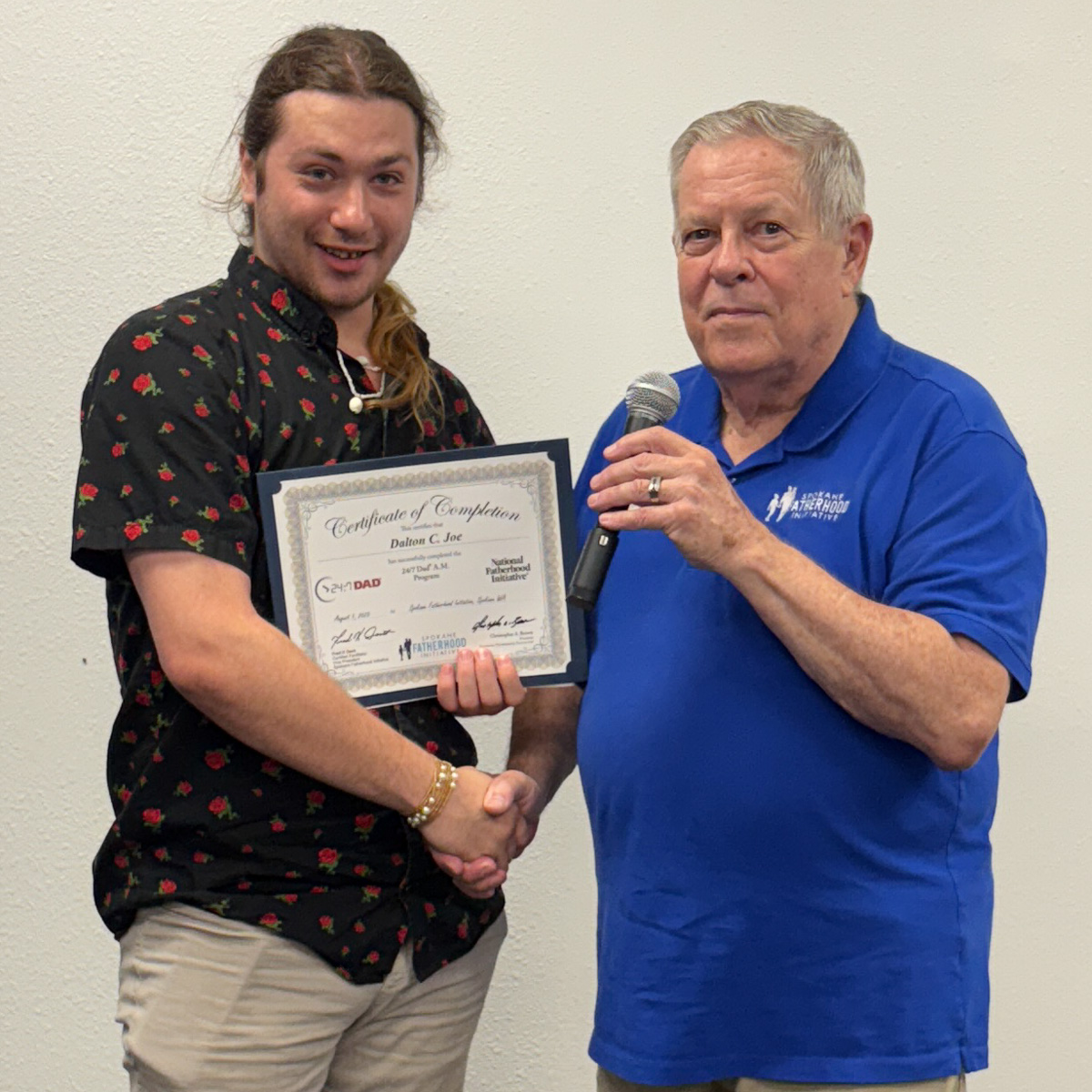 18 Spokane fathers graduate from 24-7 Dad® program: Another milestone in strengthening Spokane families 6 Young father with long hair in rose-patterned shirt receiving certificate from instructor