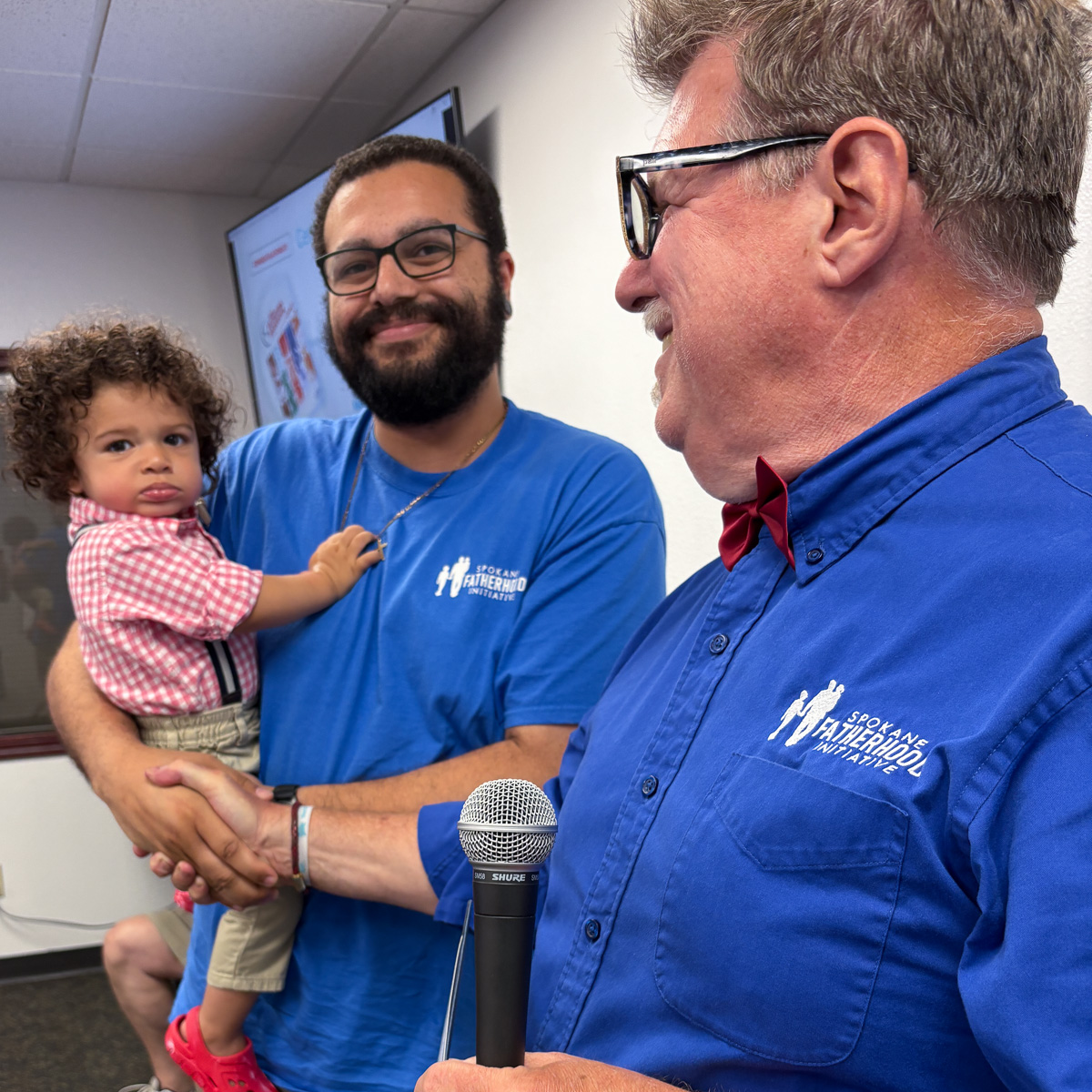 Mixed-race father holding toddler in checkered dress shirt during graduation ceremony