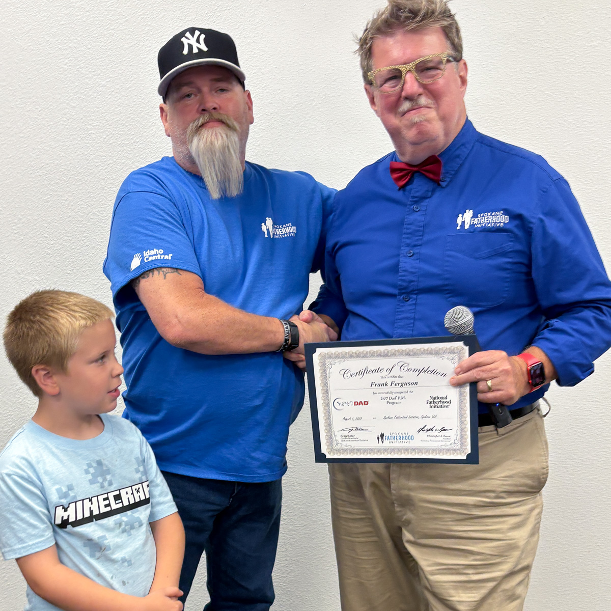 18 Spokane fathers graduate from 24-7 Dad® program: Another milestone in strengthening Spokane families 13 Father in Yankees cap and blue SpoFI shirt with young son, receiving certificate from instructor
