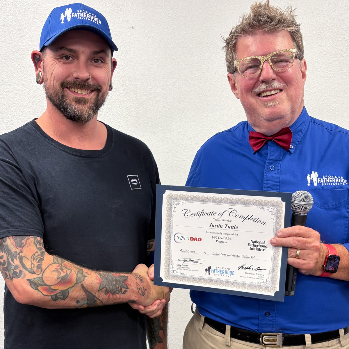 18 Spokane fathers graduate from 24-7 Dad® program: Another milestone in strengthening Spokane families 16 Tattooed father in black shirt shaking hands with instructor while holding graduation certificate