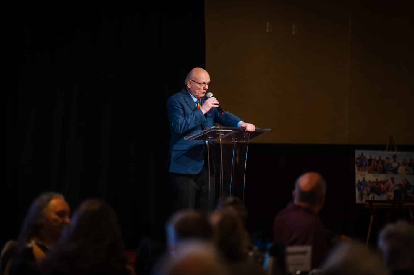 Ron Hauenstein speaks into a microphone at a clear lectern during the Spokane Fatherhood Initiative 10-year celebration opening.