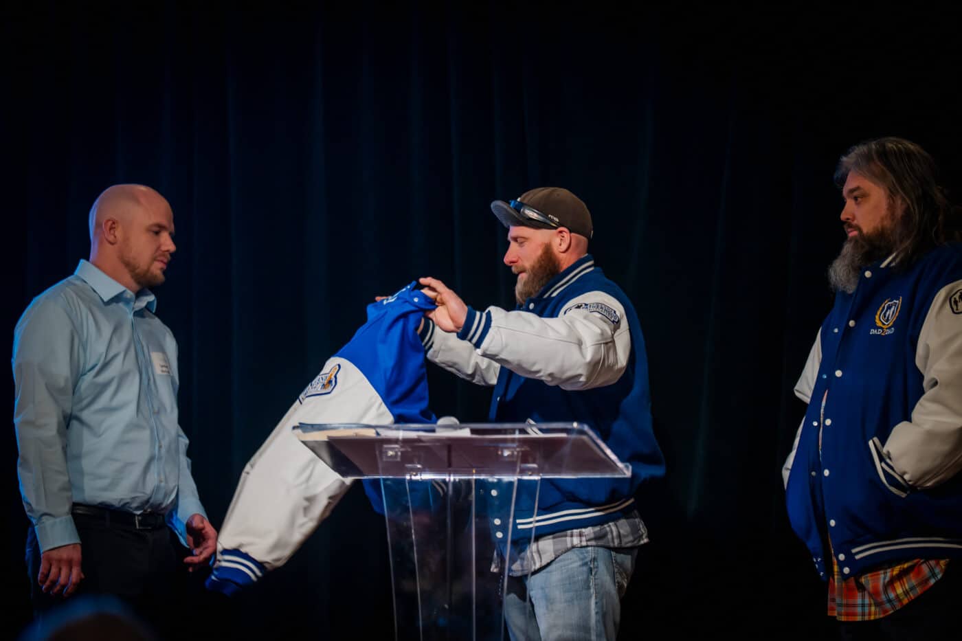Bryan Mochel holds a blue varsity jacket to present to Spencer Metcalfe at the podium.