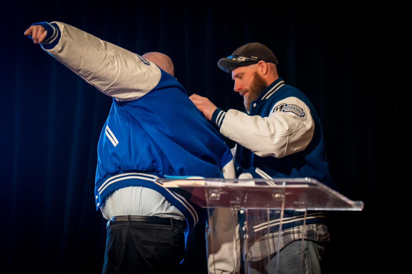 Bryan Mochel helps Spencer Metcalfe put on his Dad2Dad varsity jacket onstage.