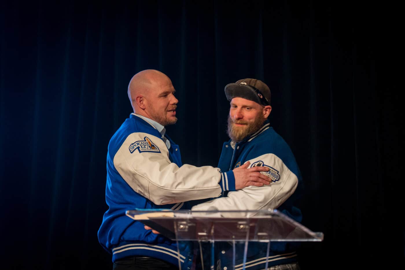 Bryan Mochel and Spencer Metcalfe stand together onstage in matching Dad2Dad varsity jackets.