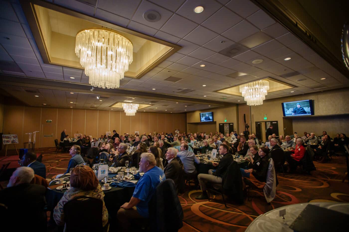 A full banquet room watches the founding story video on large screens during the SpoFI event.