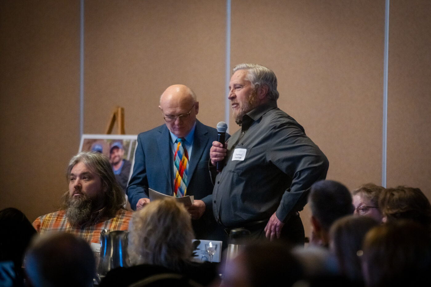 Darrel Startin stands with microphone and speaks to the room while Fred Dent stands beside him at the SpoFI 10th anniversary celebration.