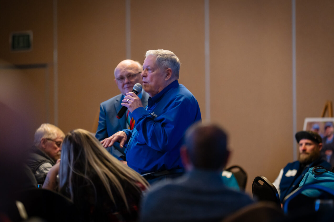 Fred Dent speaks into a microphone while Ron Hauenstein stands beside him at the SpoFI 10th anniversary celebration.