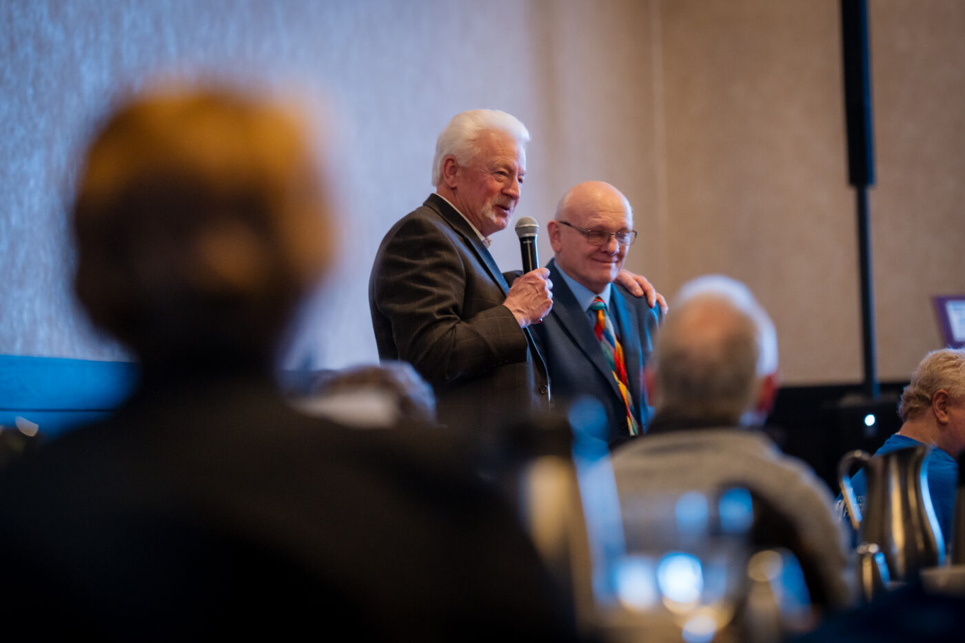 Carl Tompkins stands with Ron Hauenstein and addresses the room at the SpoFI 10th anniversary celebration.