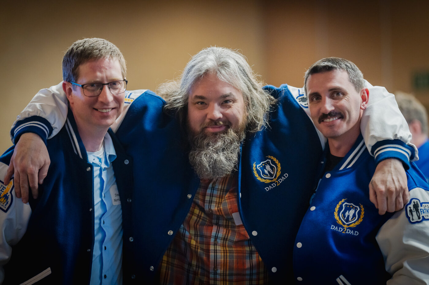 Three Dad2Dad graduates and Fathers of the Year pose together in varsity jackets - DJ Merriam, Jim Uttke, and Courtney Garnett celebrate at the SpoFI 10th anniversary.