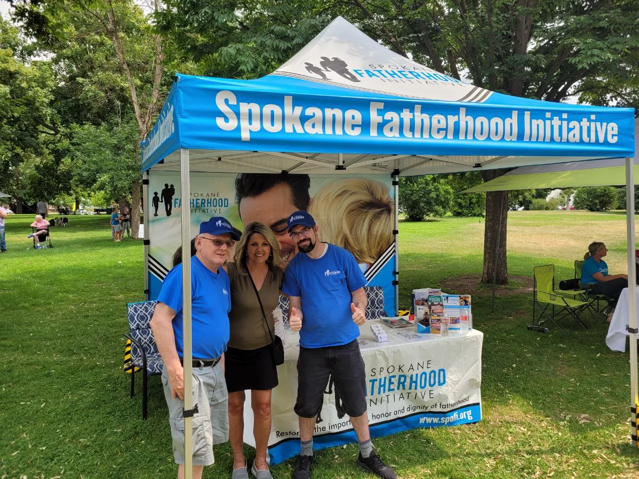 Mayor Nadine Woodward poses with SpoFI Director Ron Hauenstein and 24-7 Dad Cameron Deitz in SpoFI booth at Family Day 2024.