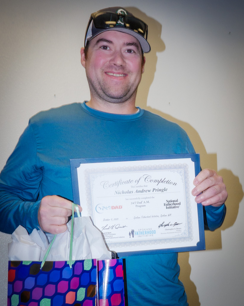Graduate Nicholas Andrew Pringle holds his 24/7 Dad® A.M. Certificate of Completion and a gift bag during the October 2025 Spokane Fatherhood Initiative graduation celebration.
