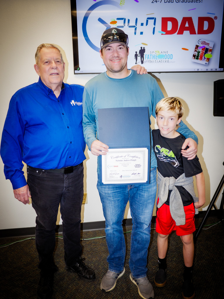 Fred Dent stands beside Nicholas Pringle and his young son as they proudly hold the 24/7 Dad certificate.