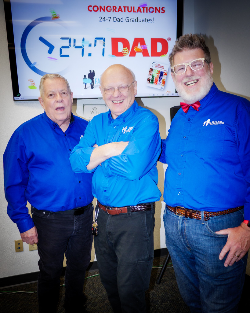 Ron Hauenstein, Fred Dent, and Greg Naker stand together in front of a “Congratulations 24/7 Dad Graduates!” screen, all wearing matching SpoFI shirts.