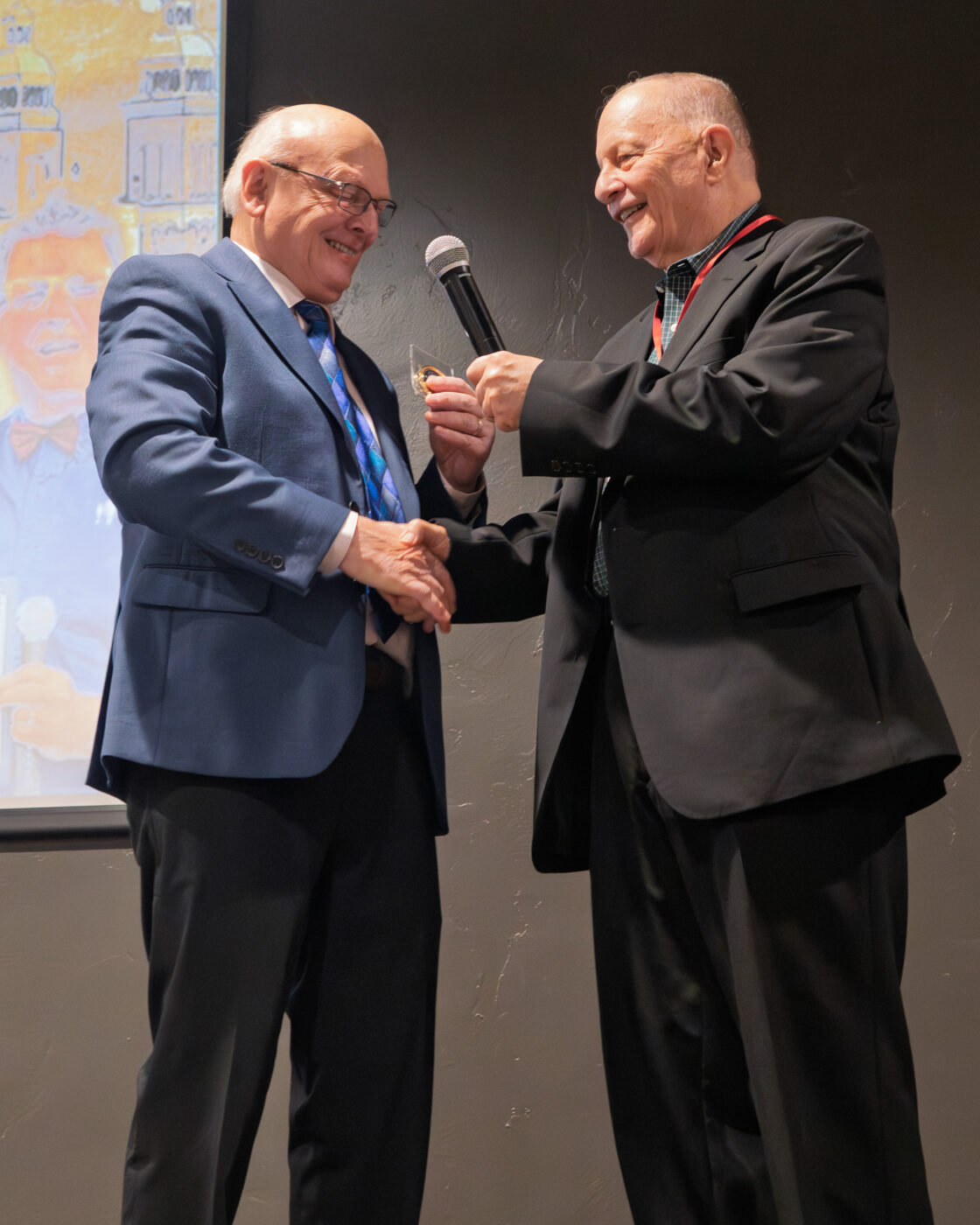 Building Legacy: Nearly 200 Gather to Celebrate Fatherhood and Family Transformation 4 Former state senator Mike Padden presents recognition award to SpoFI Executive Director Ron Hauenstein on stage as both men shake hands and smile