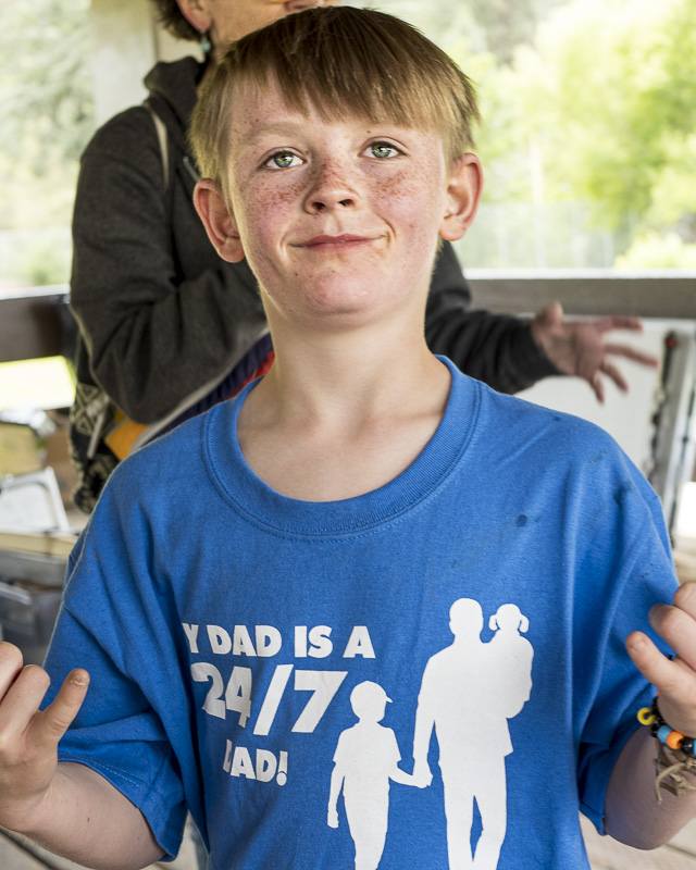 SpoFI Alumni: Step Up and Lead – June 15th Picnic 3 Smiling young boy wearing blue SpoFI shirt with 'MY DAD IS A 24/7 DAD!' text and silhouettes of a father with children, proudly supporting his dad at the Father's Day picnic event