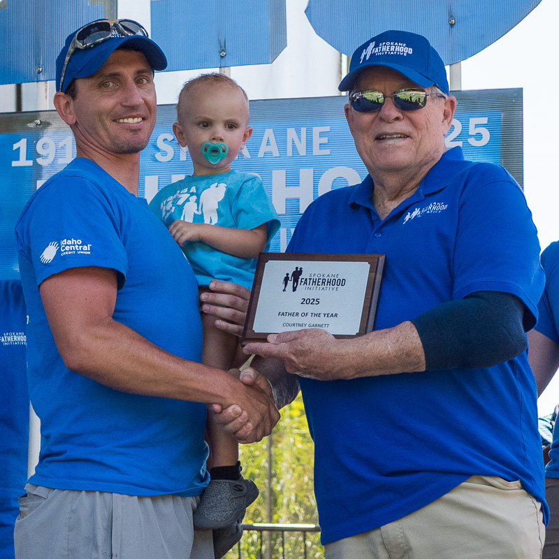Community connection strengthens Spokane families at Father's Day celebration 15 Courtney Garnett receives 2025 Non-Custodial Father of the Year award from SpoFI VP Fred Dent while holding his baby, with 115th anniversary banner behind them at Father's Day celebration