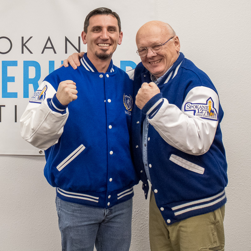 Celebrating fathers across our community this Father's Day 2 Ron Hauenstein, Executive Director of Spokane Fatherhood Initiative, and Courtney G, 2025 Father of the Year recipient, wearing matching blue and white Dad2Dad program letterman jackets while celebrating Father's Day achievements, both men smiling and making celebratory fist gestures